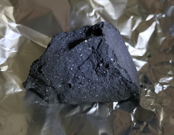 Dark grey meteorite resting on aluminium foil