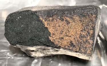 Meteorite sample showing fusion crust and dark, broken surface